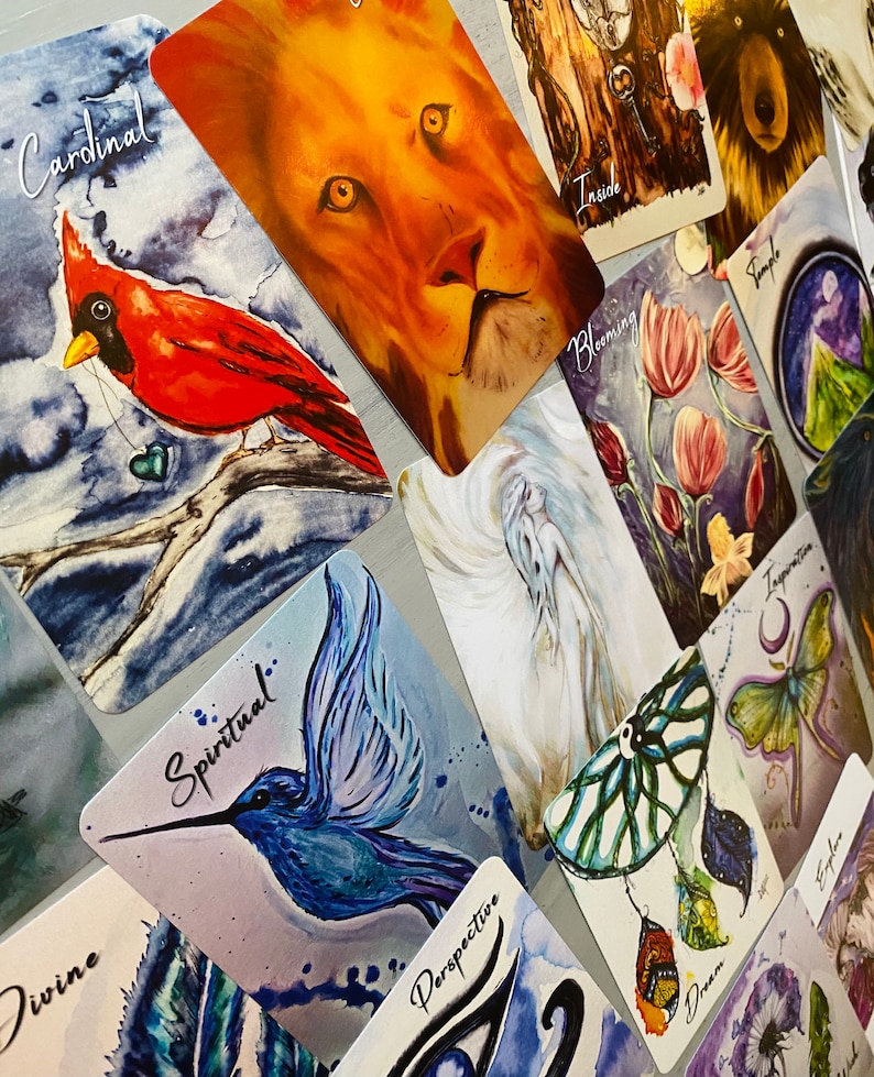 K&ouml;nnte beinhalten: Ein Set farbenfroher Orakelkarten mit verschiedenen Bildern, darunter ein Kardinal, ein L&ouml;we, ein Kolibri, ein Traumf&auml;nger und ein Tempel. Die Karten tragen Titel wie "Kardinal", "Spirituell", "Perspektive", "Traum" und "Tempel".