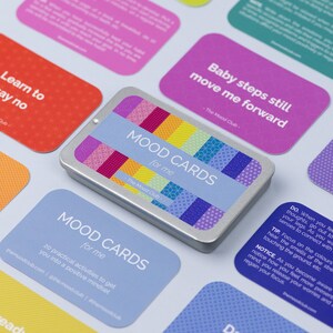 Peut inclure: Un jeu de cartes d'humeur dans une bo&icirc;te en argent avec un motif color&eacute;. Les cartes sont bleues, jaunes et blanches avec le texte "MOOD CARDS for me" imprim&eacute; dessus. La bo&icirc;te porte le texte "The Mood Club" imprim&eacute; dessus.