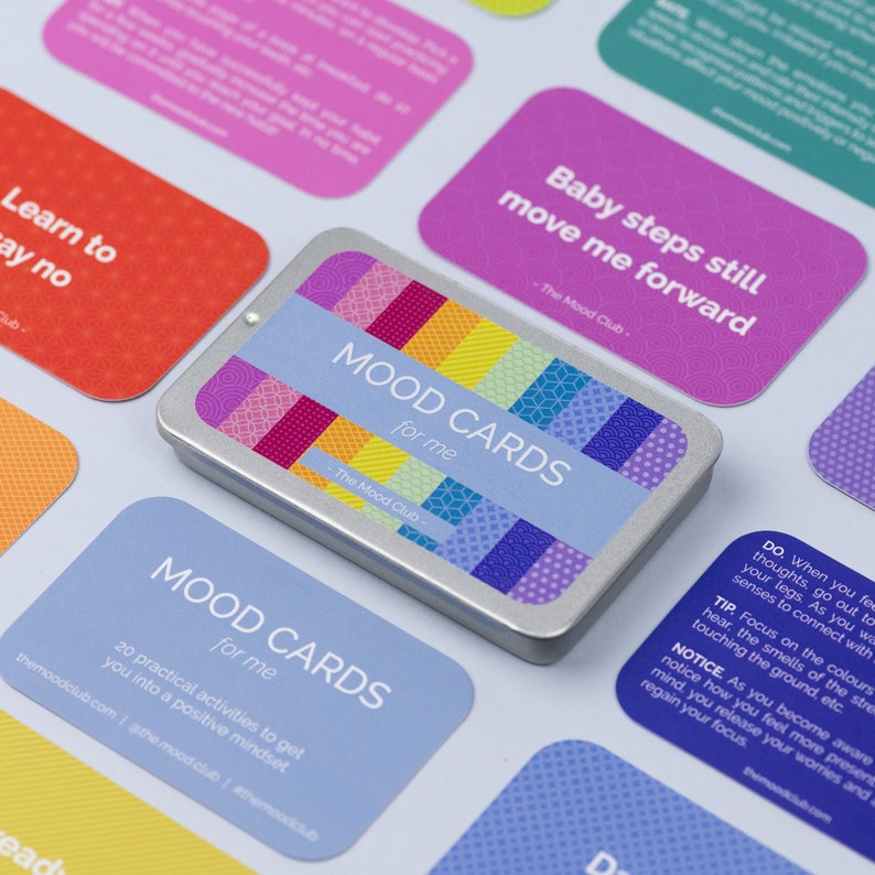 Peut inclure: Un jeu de cartes d'humeur dans une bo&icirc;te en argent avec un motif color&eacute;. Les cartes sont bleues, jaunes et blanches avec le texte "MOOD CARDS for me" imprim&eacute; dessus. La bo&icirc;te porte le texte "The Mood Club" imprim&eacute; dessus.