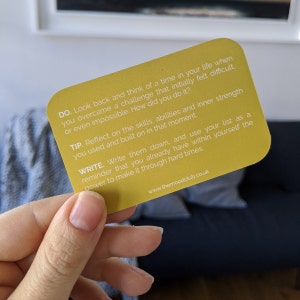 Peut inclure: Carte jaune avec une citation motivante sur le d&eacute;passement des d&eacute;fis. Elle dit "DO. Look back and think of a time in your life when you overcame a challenge that initially felt difficult or even impossible. How did you do it? TIP. Reflect on the skills, abilities and inner strength you used and built on in that moment. WRITE. Write them down, and use your list as a reminder that you already have within yourself the power to make it through hard times. www.themoodclub.co.uk"