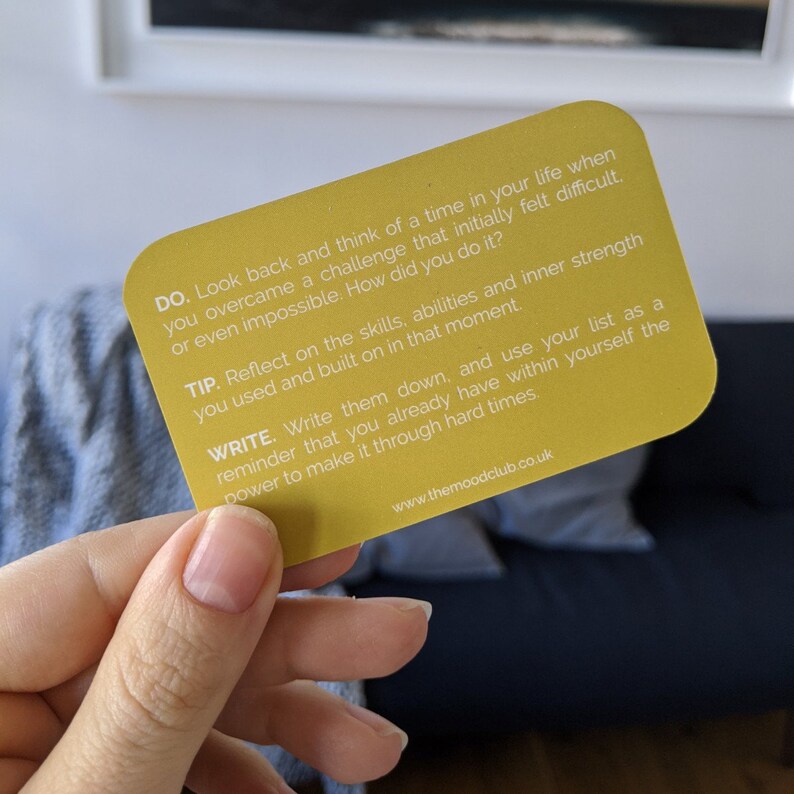 Peut inclure: Carte jaune avec une citation motivante sur le d&eacute;passement des d&eacute;fis. Elle dit "DO. Look back and think of a time in your life when you overcame a challenge that initially felt difficult or even impossible. How did you do it? TIP. Reflect on the skills, abilities and inner strength you used and built on in that moment. WRITE. Write them down, and use your list as a reminder that you already have within yourself the power to make it through hard times. www.themoodclub.co.uk"
