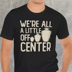 Może przedstawiać: Czarny t-shirt z białym nadrukiem, na którym widnieje napis "We're all a little off center" i szereg czterech stylizowanych urn.