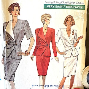 May include: Vogue Patterns sewing pattern featuring illustrations of women's suits. The pattern includes the text "VERY EASY" and size information. A red spool of thread and a black and tan spool are visible.