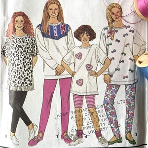 May include: Simplicity sewing pattern packet featuring illustrations of women's clothing designs. The packet is white with black text and includes a barcode and the number 8499. Spools of pink, white, and blue thread are visible.