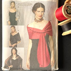 Puede incluir: Un patrón de costura vintage de Vogue Accessories, con una mujer con un chal rojo sobre un vestido negro. El patrón incluye múltiples vistas y tallas. Se ven carretes de hilo rojo y negro.