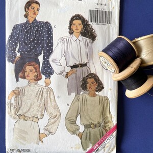 May include: A vintage Butterick sewing pattern, number 5714, with blouse designs. The pattern includes sizes 12-14-16. The cover shows blouse illustrations with long sleeves and belts. Includes spools of thread.