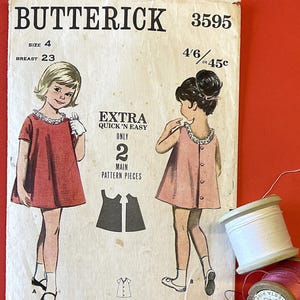 May include: Vintage Butterick sewing pattern 3595 for a girl's dress, size 4, with a 23-inch breast measurement. The pattern features illustrations of the dress and includes the text "EXTRA QUICK 'N EASY." Spools of thread in white and pink are also visible.