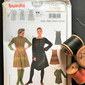May include: Burda sewing pattern number 8001 for a dress. The pattern includes three different styles: a tiered dress, a dress with a gathered skirt, and a dress with a fitted bodice and a flared skirt. The pattern is printed on white paper with black and red text. The pattern is for sizes 8-18.