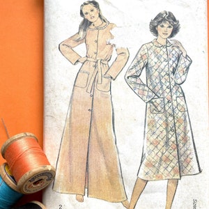 Puede incluir: Un patrón de costura vintage para una bata larga con botones y cinturón de lazo. El patrón es de New Look, una marca popular de patrones de costura, y es para las tallas 10-18. El patrón presenta dos estilos diferentes de batas, una con un color sólido y otra con un estampado floral.