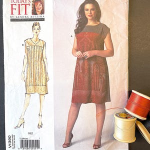 May include: A sewing pattern titled "Today's Fit" by Sandra Betzina. The pattern features a dress design with a model wearing the dress. Spools of thread and a seam ripper are next to the pattern. The pattern number is V1390.