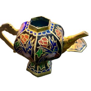 May include: A miniature decorative teapot with a gold handle and spout. The body is black with floral and bird designs in red, blue, and green, outlined in gold. The teapot sits on a gold base.
