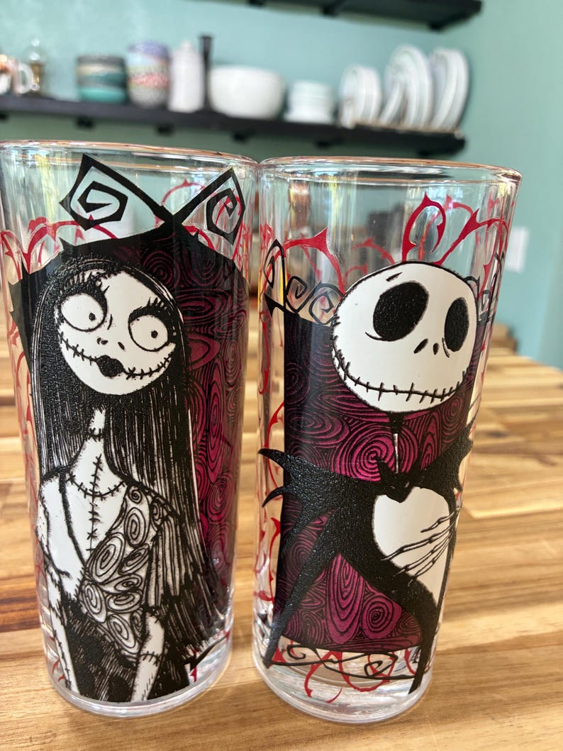 Puede incluir: Dos vasos transparentes con ilustraciones de personajes en blanco y negro. El vaso izquierdo muestra una figura femenina con cabello largo y detalles de costuras. El vaso derecho muestra una figura esquel&eacute;tica con cabeza redonda y pajarita.