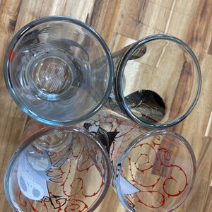 Puede incluir: Cuatro vasos de cristal transparente vistos desde arriba, con dise&ntilde;os impresos de un personaje esquel&eacute;tico y patrones de enredaderas rojas. Los vasos tienen bordes circulares y paredes transparentes que muestran los gr&aacute;ficos internos.