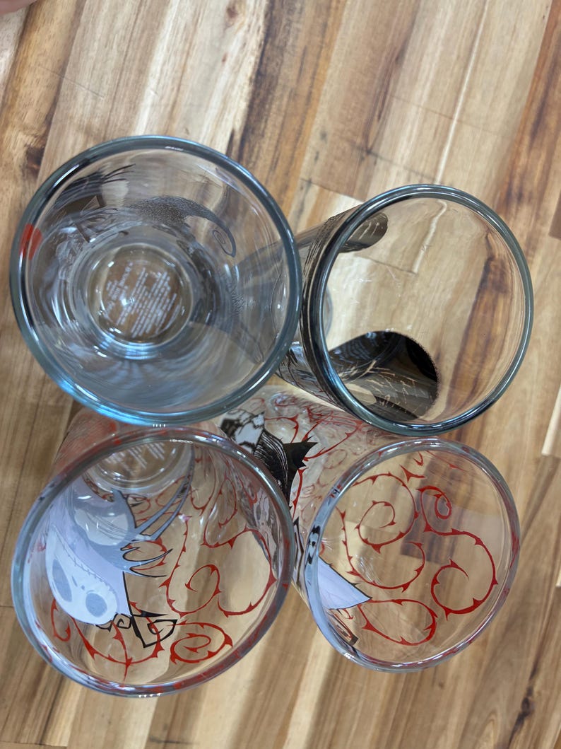 Puede incluir: Cuatro vasos de cristal transparente vistos desde arriba, con dise&ntilde;os impresos de un personaje esquel&eacute;tico y patrones de enredaderas rojas. Los vasos tienen bordes circulares y paredes transparentes que muestran los gr&aacute;ficos internos.