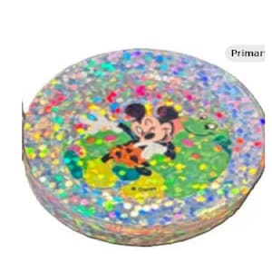 May include: A round, glitter-filled object featuring a cartoon image of Mickey Mouse and a green frog. The design includes colorful confetti and the word "Primar". The object has a Disney copyright.