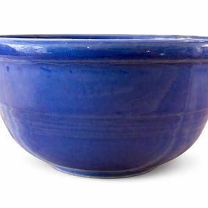 May include: A round, deep blue ceramic bowl with a glossy finish. The bowl has a wide rim and a slightly textured surface. The bowl is approximately 10 inches in diameter and 5 inches deep, suitable for serving or display.