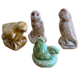 May include: A collection of four small ceramic animal figurines featuring a glossy finish. The set includes a golden-brown bird, a light brown owl, a pale brown hawk, and a light green rooster, each sculpted in a seated or standing position.
