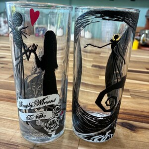 Puede incluir: Dos vasos de cristal transparente con ilustraciones de siluetas negras. Uno muestra dos figuras tomadas de la mano con un coraz&oacute;n rojo y el texto Simply Meant To Be. El otro vaso muestra una figura solitaria dentro de un marco negro giratorio.