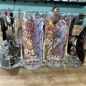 Puede incluir: Cuatro vasos de vidrio transparente con ilustraciones de personajes en blanco y negro y patrones de enredaderas rojas. Los dise&ntilde;os incluyen siluetas de una figura alta y delgada y una figura femenina, una cara esquel&eacute;tica y l&iacute;neas negras.