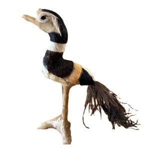 May include: A decorative bird figurine with a long neck and legs. The bird features a head with a light brown beak and a body with black, white, and tan stripes. The tail is made of dark brown feathers.