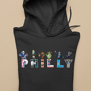 Könnte beinhalten: Schwarzer Hoodie mit dem Wort "PHILLY", das in bunten Teamlogos und Maskottchen der professionellen Sportteams aus Philadelphia geschrieben ist.