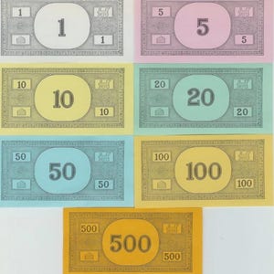 以下が含まれることがあります： カラフルなモノポリー紙幣のコレクション。1、5、10、20、50、100、500の額面があります。各紙幣には、大きな円の中にその価値が表示され、隅には小さな価値が表示されています。