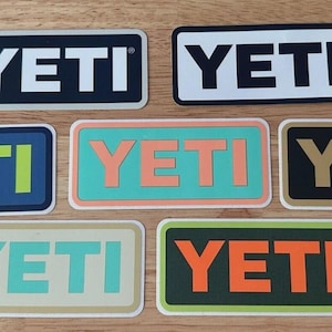 以下が含まれることがあります： YETIのブランド名が記された7枚の長方形ステッカーのコレクション。黒地に白文字、白地に黒文字、青地にライムグリーン文字、ティール地にピーチ文字、黒地にゴールド文字、クリーム地にティール文字、ダークグリーン地にオレンジ文字など、様々な色の組み合わせがあります。