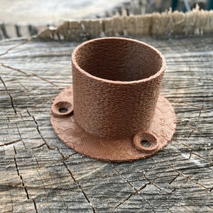 May include: A brown plastic 3D printed pipe fitting with a round base and two holes. The fitting has a textured surface.
