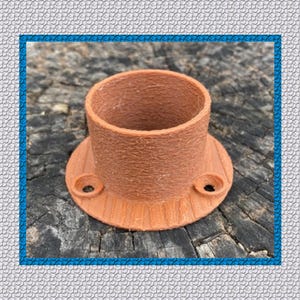 May include: A terracotta-colored, cylindrical object with a wide, flat base and two small holes. The object has a textured surface and appears to be made of a composite material. The base has a ridged design. The object is sitting on a weathered wooden surface.