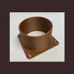 May include: A brown, cylindrical object with a textured surface, mounted on a square base. The base has four holes, likely for screws or bolts. The object appears to be made of plastic or a similar material.