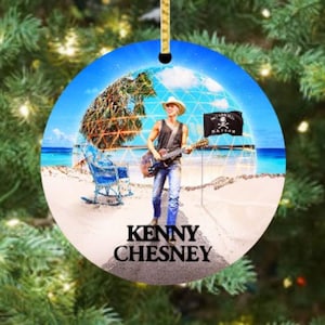 May include: Round Christmas ornament featuring a beach scene with a musician playing a guitar. The ornament has a blue sky background and the text "Kenny Chesney" in white. A black flag with a skull and crossbones is also visible.