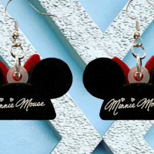May include: A pair of black Minnie Mouse earrings. Each earring features a black mouse ear design with a red bow and the words "Minnie Mouse" in cursive. The earrings have silver-colored hooks.