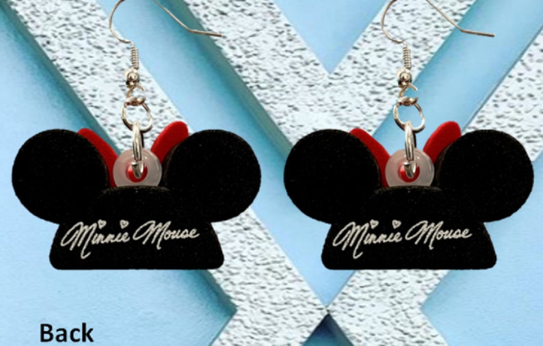 May include: A pair of black Minnie Mouse earrings. Each earring features a black mouse ear design with a red bow and the words "Minnie Mouse" in cursive. The earrings have silver-colored hooks.