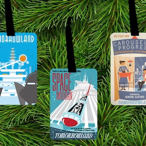 May include: Three Tomorrowland-themed Christmas ornaments. The ornaments feature retro-style illustrations of Space Mountain, Carousel of Progress, and Tomorrowland attractions. Each ornament has a black ribbon for hanging, set against a backdrop of green pine needles.