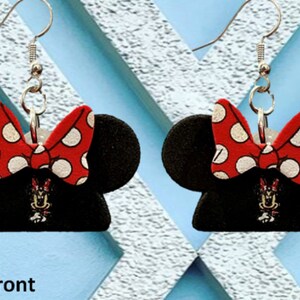 May include: A pair of black Minnie Mouse-themed earrings. Each earring features a black mouse ear silhouette with a red bow with white polka dots. A small Minnie Mouse graphic is visible below the bow.