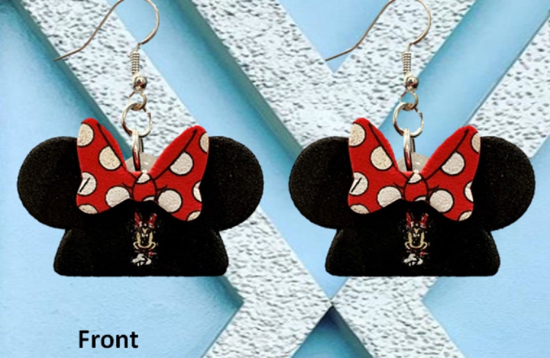 May include: A pair of black Minnie Mouse-themed earrings. Each earring features a black mouse ear silhouette with a red bow with white polka dots. A small Minnie Mouse graphic is visible below the bow.