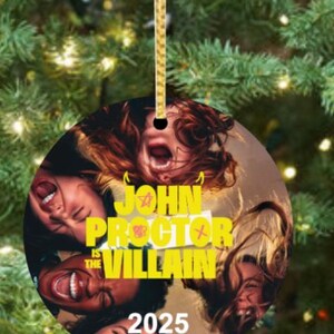 Puede incluir: Adorno navide&ntilde;o redondo con una cuerda dorada. Presenta un collage de caras con la boca abierta y el texto "JOHN PROCTOR IS THE VILLAIN 2025" en amarillo.