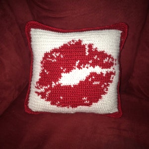Peut inclure: Un coussin crocheté blanc avec un motif de lèvres crocheté rouge.