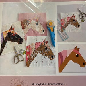 May include: A sewing pattern package titled Happy Horse Quilt Block by Liz Taylor Handmade. The cover displays multiple fabric horse head designs in various floral and solid prints, alongside a rotary cutter, scissors, and a ruler.