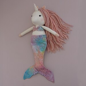 May include: A handmade unicorn mermaid doll with a white face, a spiral horn, and pink yarn hair. The doll has a pink and blue tie-dye mermaid tail and a matching top. The doll is approximately 18 inches tall.