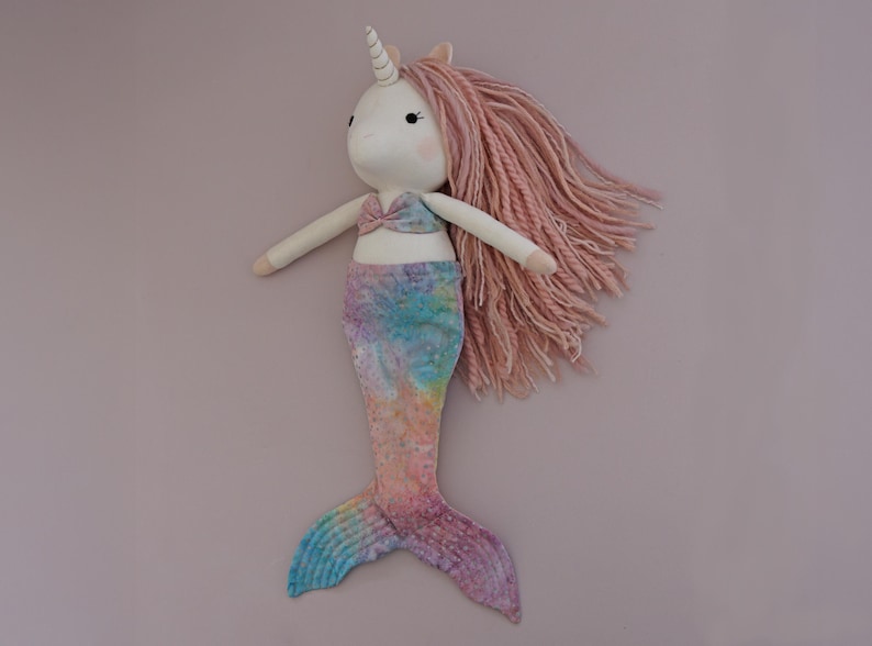 May include: A handmade unicorn mermaid doll with a white face, a spiral horn, and pink yarn hair. The doll has a pink and blue tie-dye mermaid tail and a matching top. The doll is approximately 18 inches tall.