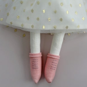 May include: A handmade doll with white fabric legs and pink felt shoes. The doll is wearing a white tulle skirt with gold polka dots.