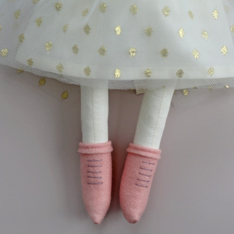 May include: A handmade doll with white fabric legs and pink felt shoes. The doll is wearing a white tulle skirt with gold polka dots.