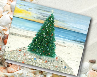 May include: A Christmas card featuring a decorated green Christmas tree on a sandy beach with the ocean and sky in the background. The tree is adorned with ornaments and a star. The card is surrounded by seashells.