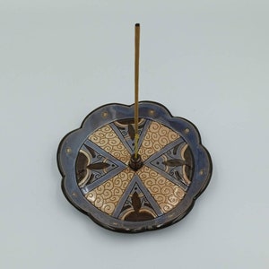 Può includere: Un porta incenso in ceramica blu e marrone con un motivo decorativo a spirale. Un singolo bastoncino di incenso è posto nel porta incenso.