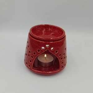 May include: Red ceramic oil burner with a small tea light candle inside. The burner has a decorative design with small holes around the sides.