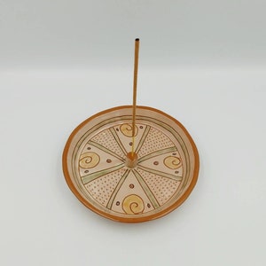 Könnte beinhalten: Ein Keramik-Räucherofen mit geometrischem Design in Braun-, Grün- und Gelbtönen. Der Räucherofen hat ein zentrales Loch für einen Räucherstäbchen, das im Lieferumfang enthalten ist.