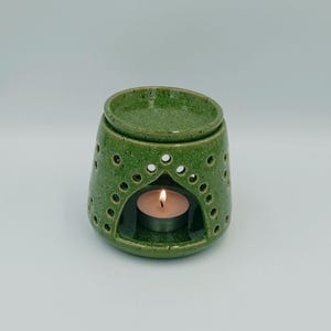 Op de afbeelding: Een groene keramische olieverdamper met een klein theelichtje erin. De diffuser heeft een decoratief ontwerp met gaten rond de bovenkant en een kleine opening in het midden voor de kaars.