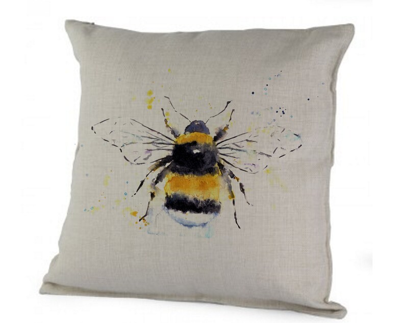 Puede incluir: Una almohada de lino beige con una pintura de acuarela de un abejorro. El abejorro es amarillo y negro con alas transl&uacute;cidas. El fondo es beige claro con salpicaduras de acuarela amarilla y azul.