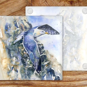 May include: A watercolor painting of a blue and white seagull perched on a rocky cliff. The seagull is in flight, with its wings spread wide. The background is a soft blue and white, with hints of yellow and green.